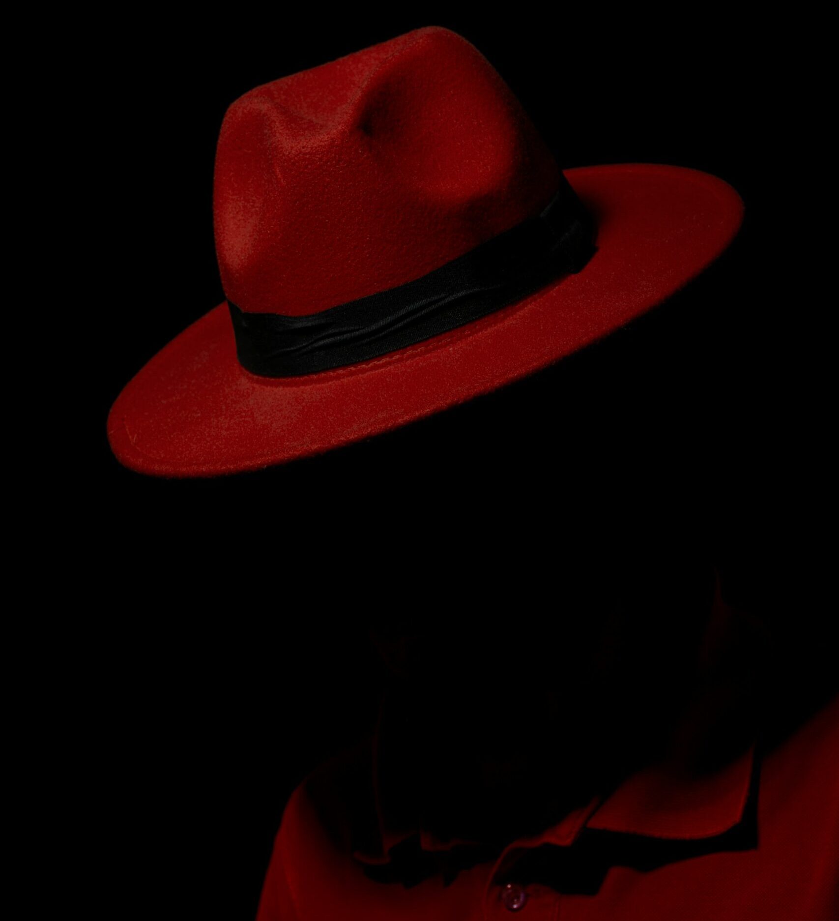 a person in a red trilby hat and coat, with their face in shadow
